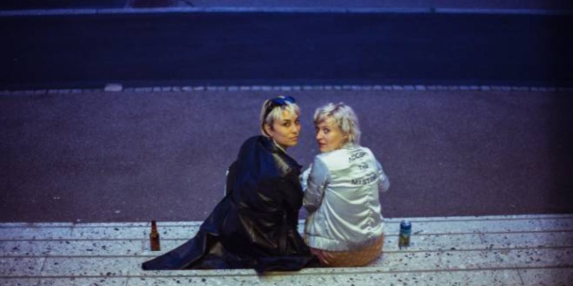 two blonde women seated on a staircase are looking behind